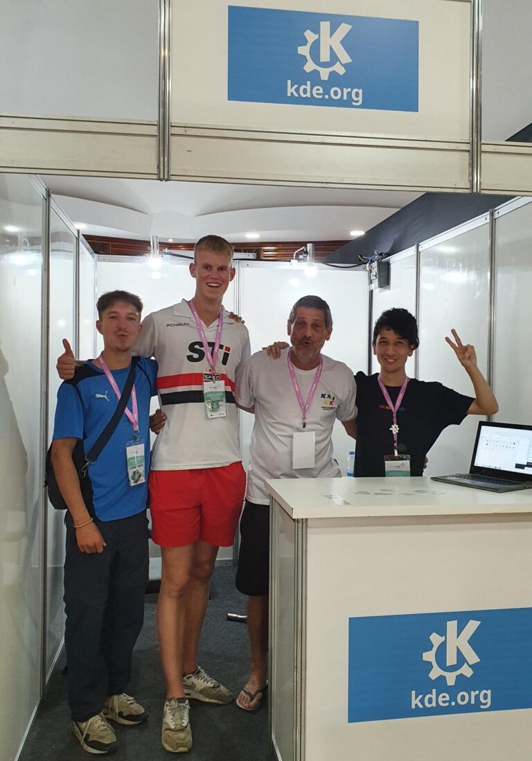 Group of four people posing in the KDE booth. The second from the left is an exceptionally tall Danish youngster.